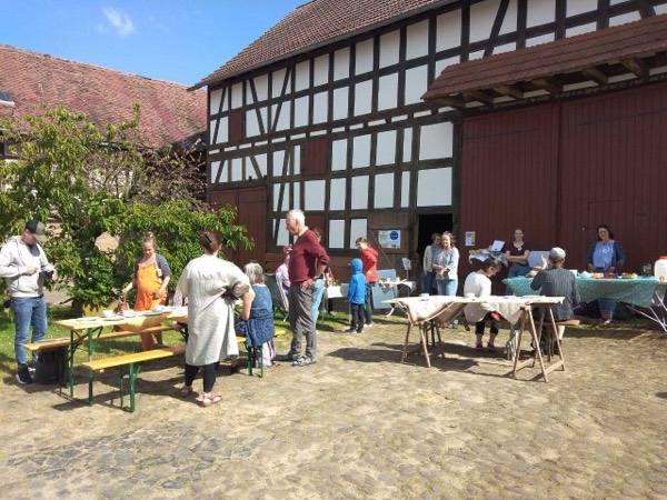 Begegnung auf einer Veranstaltung — Menschen sitzen gemeinsam an gedeckten Tischen unter Bäumen